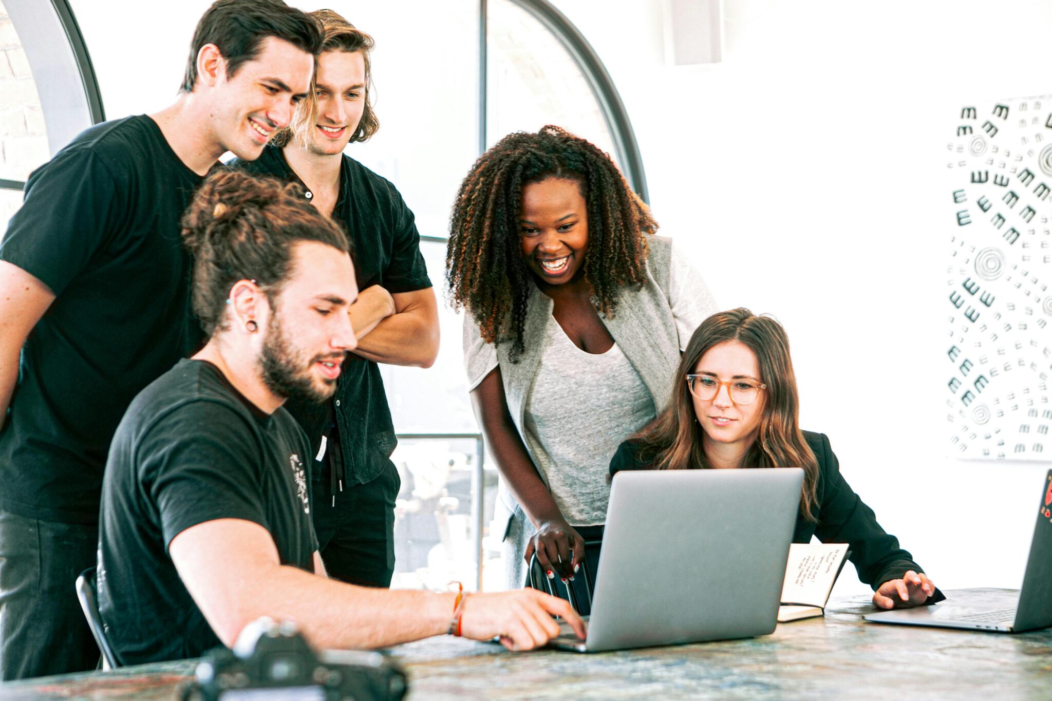 Three people smiling and looking at a laptop together in a bright office environment